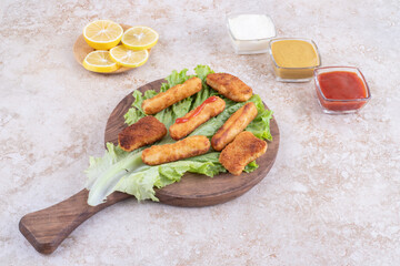 Fried chicken nuggets and grilled sausage sticks on a piece of lettuce with sauces around