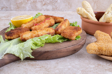 Fried chicken nuggets and cheese sticks on a wooden board on a piece of lettuce leaf