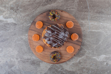 Marmelades, small donuts and a chocolate coated cake on a wooden board on marble background