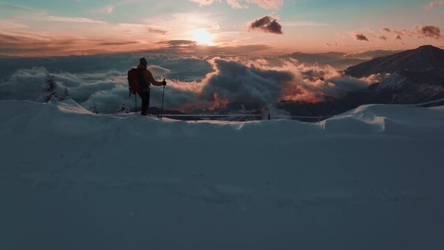 Aerial view of a young man standing on the top of a mountain slope. Watching untouched snow mountain landscape on a beautiful sunset with pink, red sky. Extreme winter expedition tour. Personal achive