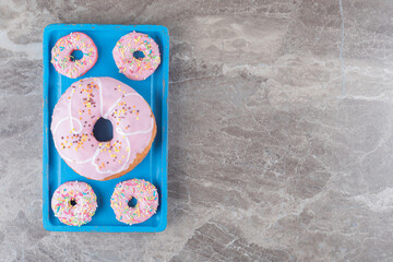 Large and small donuts arranged on a blue platter on marble background