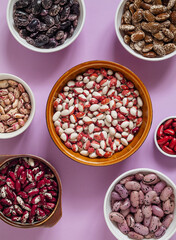 Many bowls with different heirloom beans on a purple background. Healthy eating. Top view.