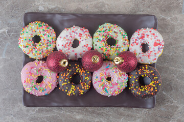 Donuts and christmas baubles arranged on a platter on marble background