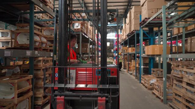 Asian worker drive flok lift to lift products in wooden crate to shelves, professional labor with safety helmet distribute goods to shelves, flok lift machine help people from overload packaging crate