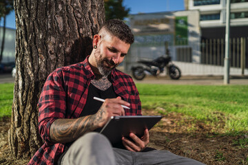 Chico joven tatuado con barba dibujando en tablet digital con su motocicleta de fondo
