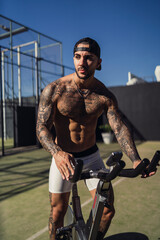 Fototapeta na wymiar Chico joven tatuado y musculoso posando y haciendo ejercicio en gimnasio al aire libre en día soleado
