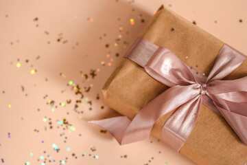 Valentines Day, Birthday or New Year present in kraft paper with pink ribbon on soft beige background with glitter and bokeh. Happy holidays celebration and giving love concept. 2022 2023 Xmas, top 