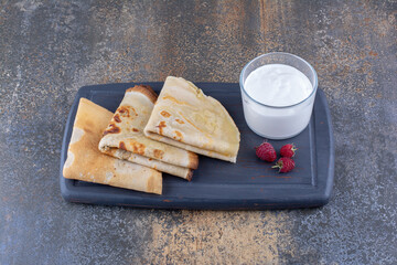 Crepes on a black platter with raspberries and a cup of milk
