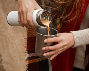 A woman pours coffee with milk into a cup from a thermos. Tourism and travel. Autumn photos.