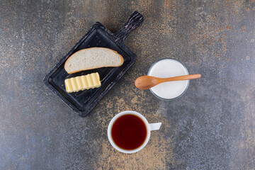 Bread, butter on a wooden board with tea and cream
