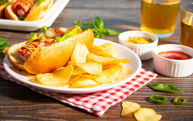 Delicious homemade hotdogs with dips sauces, chips and glasses of beer on wooden table. Top view. Copy space.