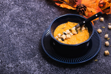 Bowl of pumpkin soup with croutons and seeds on stone kitchen counter. Copy space for your text