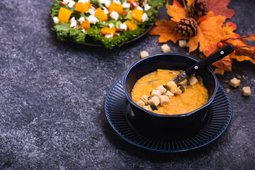 Bowl of pumpkin soup with croutons and seeds on stone kitchen counter. Copy space for your text