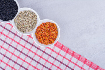 Cumin, anise seeds and saffron in white saucers on a checked towel