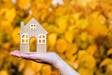 The symbol of the house in the girl's hand on the background of yellow leaves
