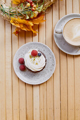 Autumn creamy tender berries cupcake with cup of cappuccino outside. Atmospheric cozy lunch at the terrace among autumn decorations