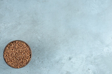 Buckwheat grains in a wooden cup on blue background