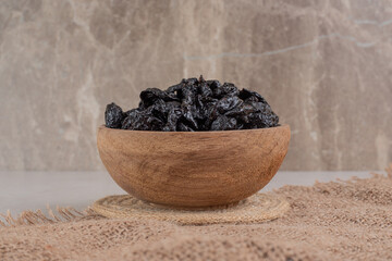 Dry black plums in a wooden cup on a piece of burlap