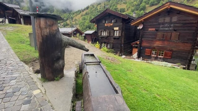 Old Water Fountain With Traditional Wooden Houses In Blatten Bei Naters Village, Switzerland. - close up