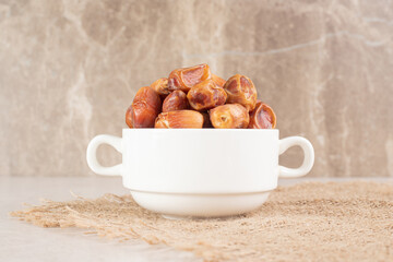 Yellow dry dates in a ceramic cup on concrete background