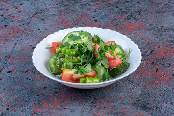 Cucumber and tomato salad mixed with parsley leaves on dark colored background