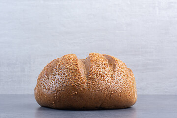 Loaf of bread covered in sesame seeds on marble background