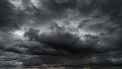 dark dramatic sky with black stormy clouds before rain or snow as abstract background, extreme weather, the sun shines through the clouds, high contrast photo