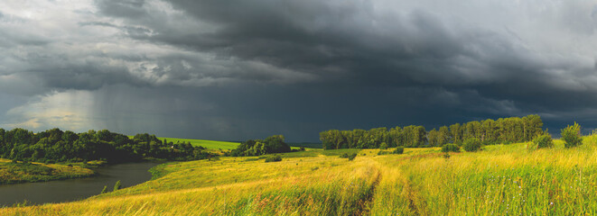 Summer rural panoramic view with calm river and dark stormy clouds over the farm fields