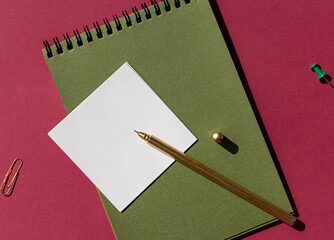 Green spiral notebook with white note paper, pen on the purple background. Copy space	