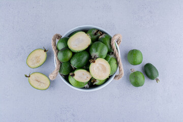 White bucket filled with fresh feijoas on marble background
