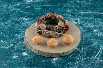 Cupcakes and a pine wreath arranged on a wooden board on blue background