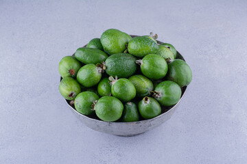 Large metal vase filled with feijoas on marble background