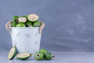 Overflowing bucket of feijoas on marble background