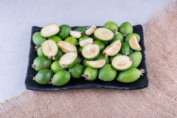 Whole and sliced feijoas on a platter on marble background