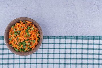 Wooden bowl of carrot salad on a tablecloth on marble background