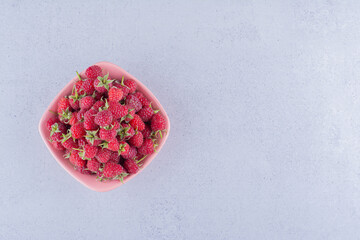 Pile of raspberries in a pink bowl on marble background