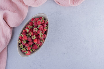 Oval bowl stocked with raspberries on marble background