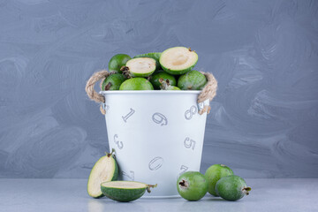 Overly filled bucket of feijoas on marble background