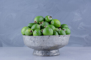 Metal vase filled with feijoas on marble background
