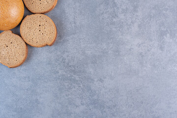 Three brown bread slices around a single bun on marble background