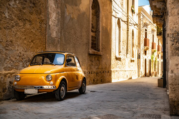 Old yellow Fiat 500 in the city centre of Syracuse in Sicily, Italy - obrazy, fototapety, plakaty