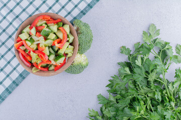Small serving of pepper and cucumber salad next to a small bundle of parsley leaves on marble background