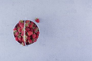 Small bucket filled with raspberries on marble background