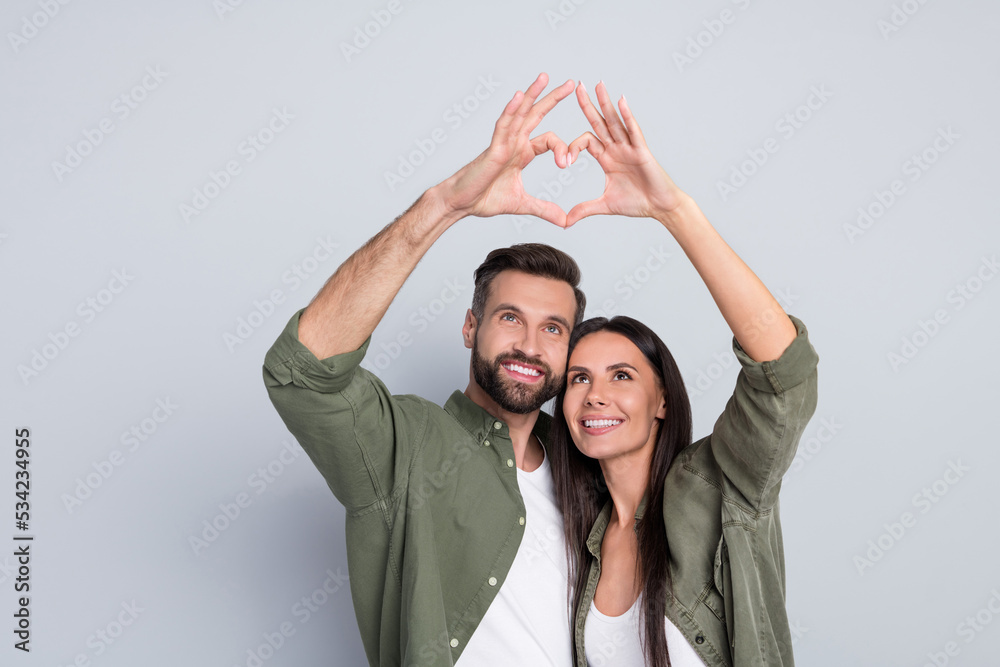 Poster portrait of attractive amorous cheerful couple hugging showing heart symbol amour isolated over grey