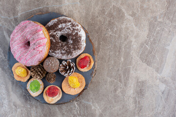 Wooden board with pine cones, marmelade topped cookies and donuts on marble background