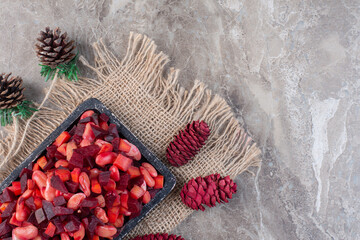 Colorful pine cones around a worn-out tray of vinegret salad on marble background