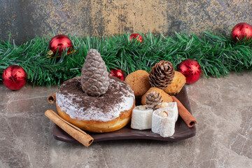 Turkish delights, cookies, cinnamon sticks and a donut in a pine cone-adorned platter on marble background