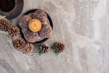 Small platter of cookies, cup of tea, bundle of pine cones and a wreath on marble background