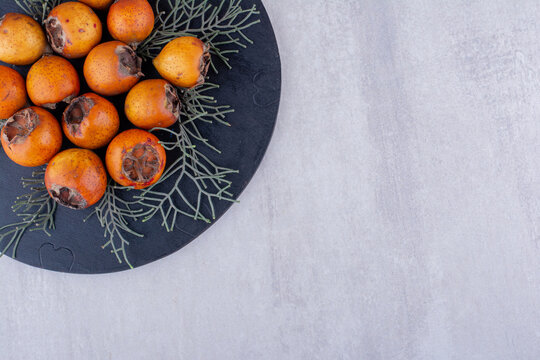 Bunch of kakis decorated with pine leaves on a board on white background