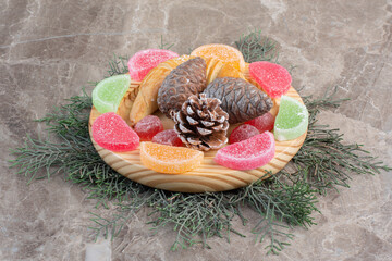 Pine cone decorated sweets platter on pine leaves on marble background